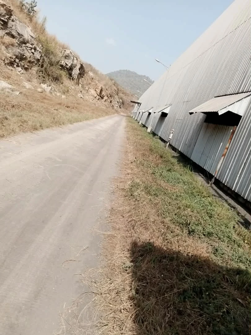 Supplied site photograph showing an access road beside an industrial building and rocky hillside