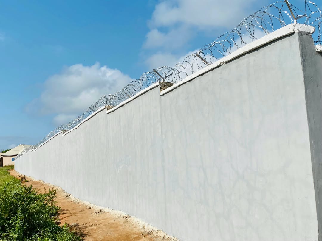 Company site photograph showing a completed painted perimeter wall with security wire topping